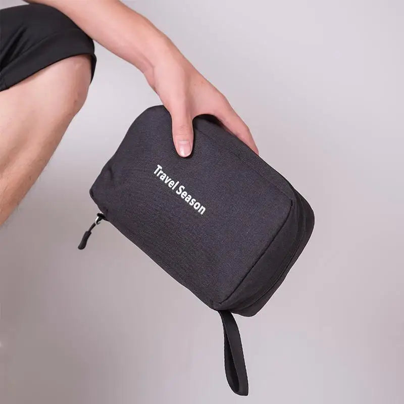 Black travel pouch with 'Travel Season' text held by a person against a neutral background