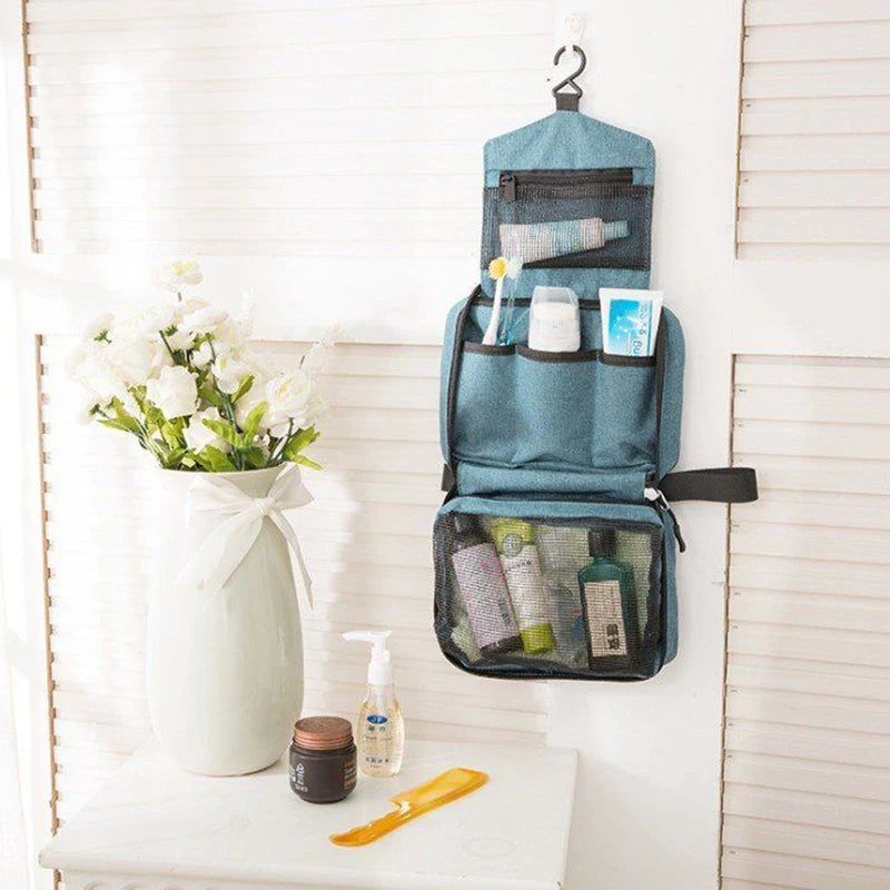 Blue hanging toiletry bag with cosmetic products on a white surface with a vase of flowers.